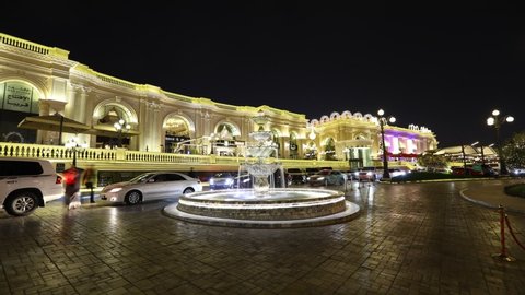 Doha, Qatar - June 28, 2019: TIMELAPSE: light trail in front of fountain at entrance of Al Hazm, shopping mall with european atmosphere. Luxury brands, shops and expansive stores with night lighting.