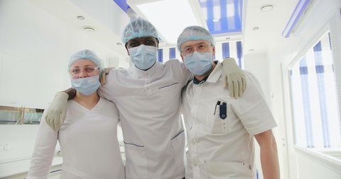 multinational colleagues dentists work together for long and are friends. black doctor hug young female nurse and european assistant in surgical masks