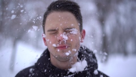 Close up of young caucasian man gets snowball on face during playing snowballs with friends, slow motion. Snowball fight. Winter fun, active leisure