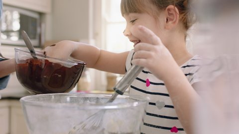 happy little girl helping mother bake in kitchen having fun mixing ingredients with mom preparing recipe at home