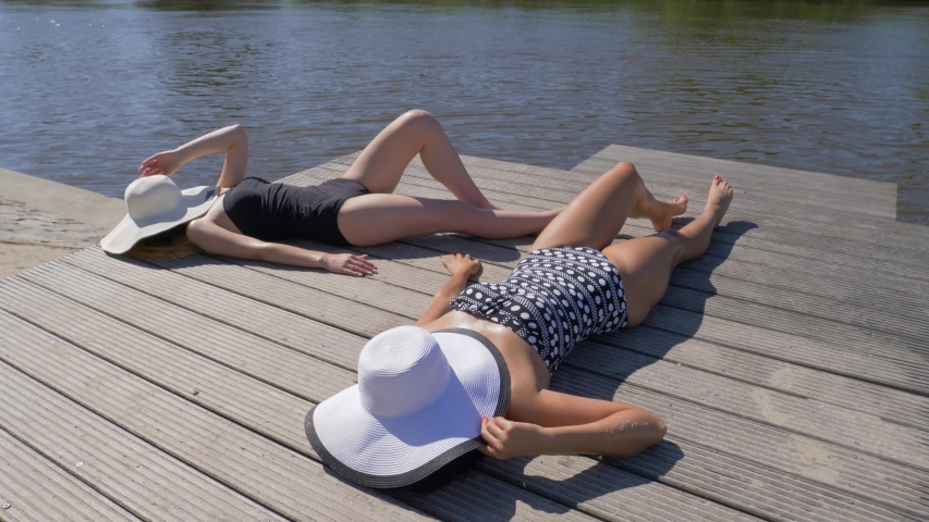 Beach leisure young girls top view lie in bikini on wooden pier tan under a sun faces covered with hats