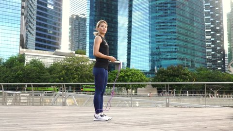Asian fitness woman doing exercises outdoors at city. Girl doing exercise with jump rope.