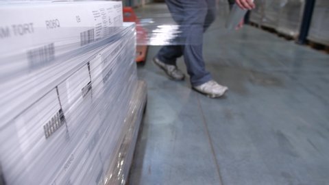 Close-up. A man is packing a pallet with boxes with plastic wrap.