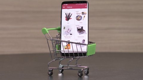 Mini shopping cart with a smartphone showing an online shop selling woman makeup items.MONTREAL, CANADA - JUNE 2019