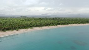 Drone video amazing tropical isle. Fly over the blue sea and palm trees forest. Aerial view white sand island beach. Palm trees, clouds and mountains background.  Top view Natural Asian forest beach 