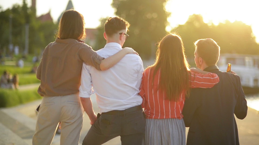 Group Of Students Staying at Park Together. Young People Cheering With Beer Bottles On Summer Time. Concept About Good And Positive Mood With Friends.