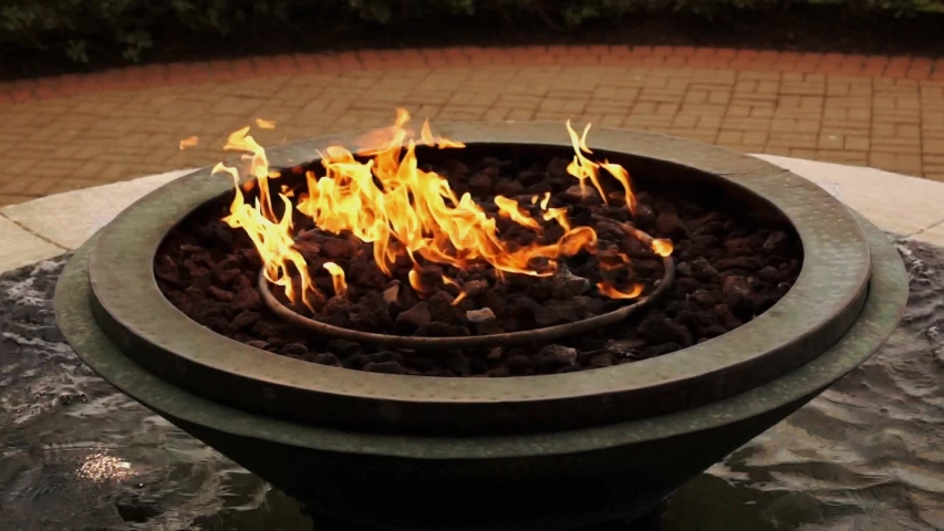 Fire burning in round fire pit sitting on a water fountain.
