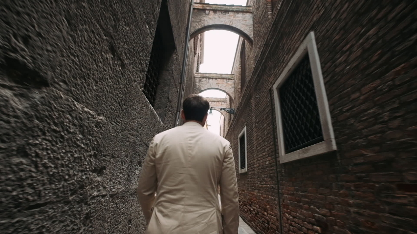 Man Goes Down A Narrow Street. Camera Goes Behind The Man.