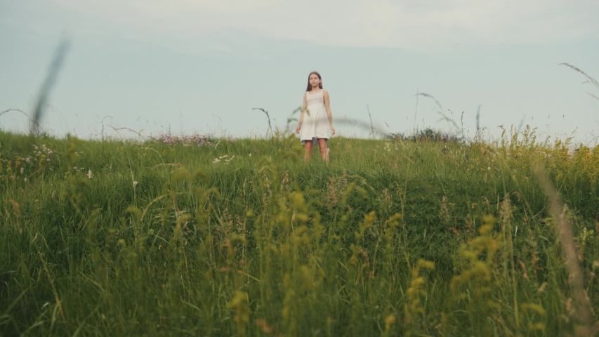 Comely teenage girl standing with raising hands in green field. Harmony. Enjoy. Positive feelings. Summertime. Outdoors. Village.