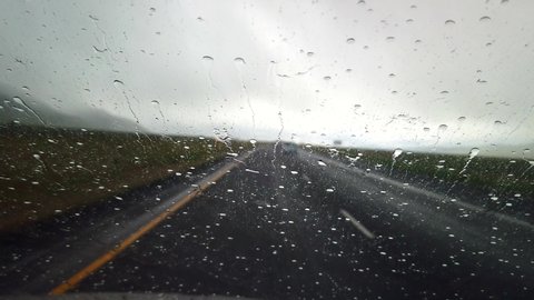 A storm is hitting the windshield of a car with the windshield wipers ring the rain drops.