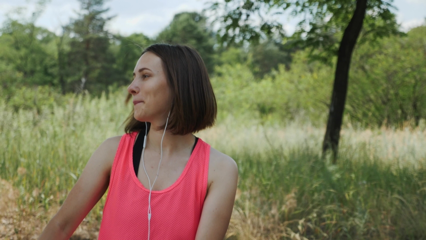 Attractive sportive girl in pink top with headphones listening music on smartphone. Slim brunette girl dancing in park. Young girl smiling to camera. Running concept. Slow motion