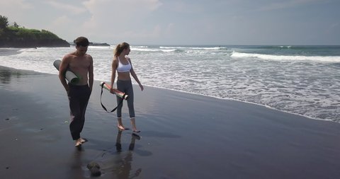 Cinematic aerial drone footage of sporty beautiful girl and handsome man walk after yoga at beach. Modern active lifestyle. Extreme on summer vacation. Yoga meditation and wellness lifestyle concept. วิดีโอสต็อก