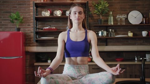 Zooming in close up view of young gorgeous fit woman sitting in lotus pose and deeply mediating, slowly breathing out and opens her eyes, looks straight to camera. Yoga time, meditation, relax