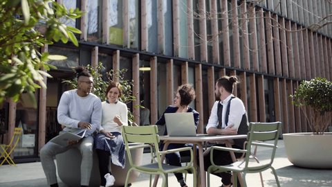 Group of young businesspeople using laptop outdoors in courtyard, start-up concept.