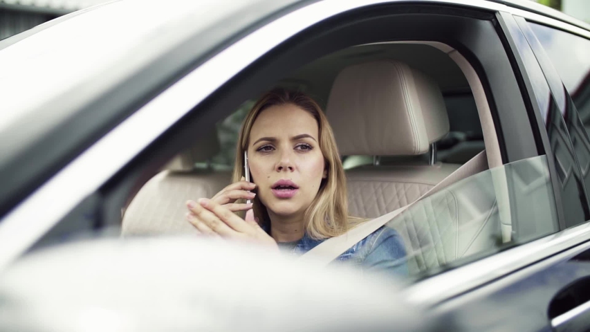 Young woman with smartphone sitting in car, making a phone call.