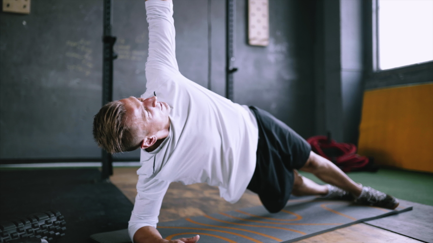 High performance triathlon or marathon exercises. Man in good fit does right side plank wraps for improving sports training. Available exercises for office workers. Intermediate no equipment. | Shutterstock HD Video #1032677474