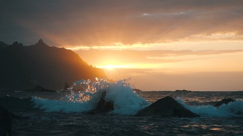 Stunning majestic waves rise in air in beautiful sunset light and sunbeams at Benijo Beach in Tenerife, Canary Islands. Picturesque large wave in ocean crashes against rocks splashes in slow motion