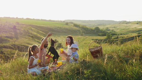 Family of four people on a picnic in the meadow at sunset. Family having fun, smiling, playing with their dog.