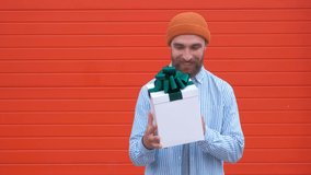 Handsome young hipster holding gift box on a red background. Concept of holidays and birthdays