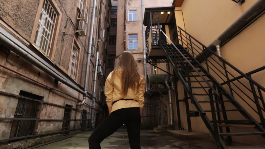 A girl stands among apartment buildings and smiles at the camera