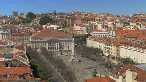 A top view of a Rossio square on a beautiful sunny day with busy everyday life happening on it. People going in different directions, cars driving along the square. There is a colorful urban view