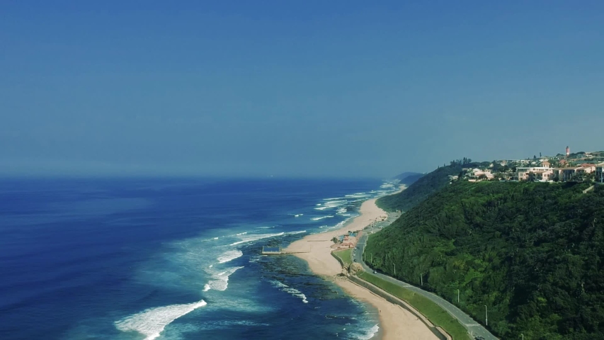 Aerial footage filmed of the Bluff Beach overlooking residential houses on a hillside then tilting down towards the beach with sea views in Durban South Africa.