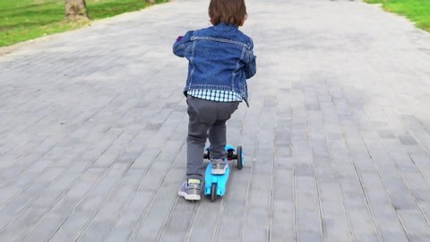 Child riding scooter on green kick board.