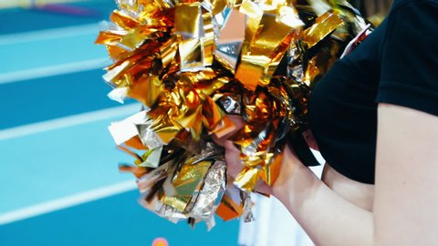 Cheerleaders pom poms glistening during sportive competition. Cheerleading pom-poms in female hands. Girl cheerleader holding pompoms during athletics championship. Motley pompoms in hands