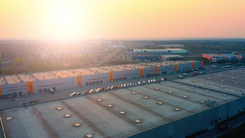 Aerial side view of logistics park with warehouse, loading hub with many semi-trailers trucks standing at the ramps for load/unload goods at sunset
