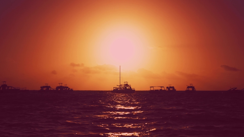 Art sunset over the sea. Yachts, waves and sunset background. Red sky sunset and yellow sun over the sea. Early morning, the yachts are preparing to go to sea. Bright red dawn and boats on horizon