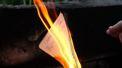 Hand drops a burning match and burning book page. Book pages are burning in fire. Bonfire of Burning Books