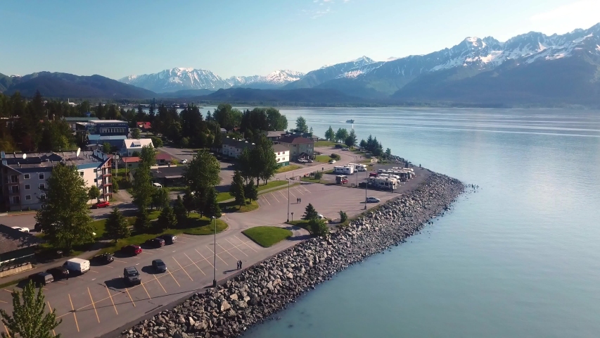 Drone aerial flight over southern shoreline of Seward, Alaska; visible are Waterfront Park, library, restaurants, hotels, houses, and parking lot; Kenai Mountains and Resurrection Bay in background