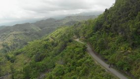 Drone follow cam of two people riding a motorcycling high up on a mountain road in the forest