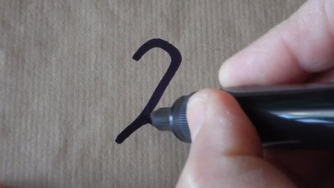 hand writes the number two 2 on wrapping paper employing a black felt tip pen