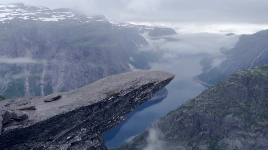Senior male hiker 50+ years old walking on a famous Trolltunga rock with a view of beautiful landscape with lake and mountains in Norway