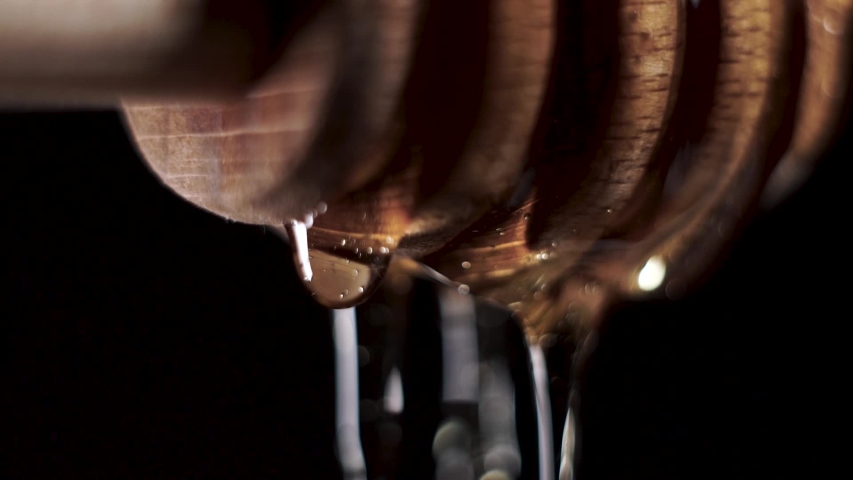 Honey falls from special honey spoon or honey dipper on black bachground