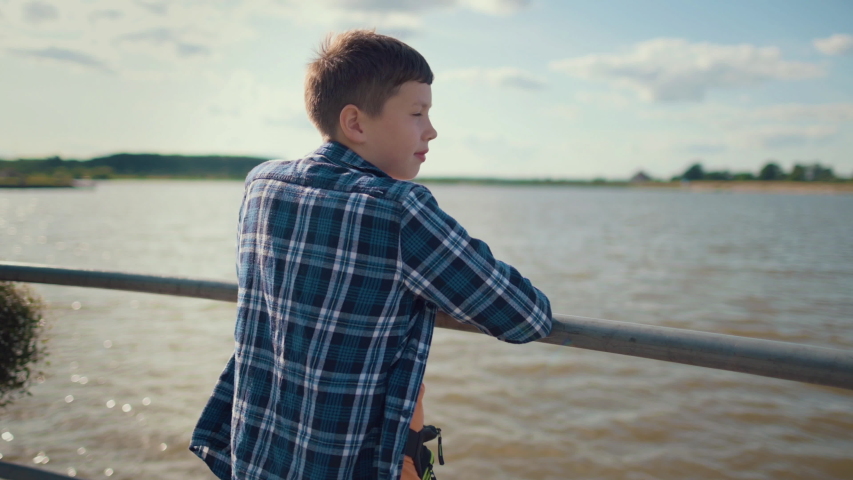 happy boy is standing on the pier near the river, shirt is developing in the wind, slow motion
