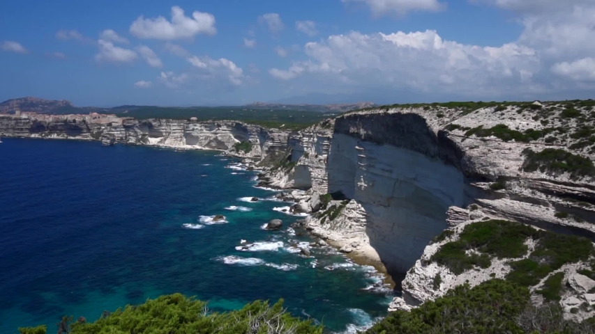 View of the unique French city of Bonifacio on the rocky cliffs of Corsica. White crumbling rocks. The landscape on the island. Blue sky and blue clear sea. Waves splitting on the rocks. slow motion