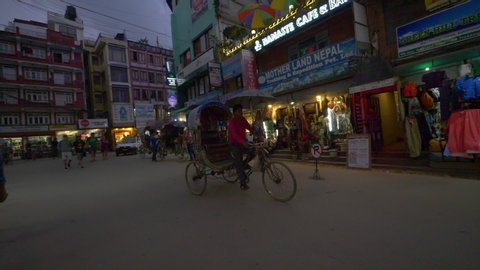KATHMANDU, NEPAL - SEPTEMBER 2018: SLOW MOTION: Locals and tourists walk and ride bikes around the touristic town in Nepal. People explore the colorful streets and souvenir shops of Kathmandu at night