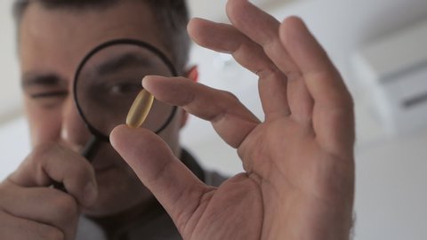 A man examines with a magnifying glass capsule with medication.
