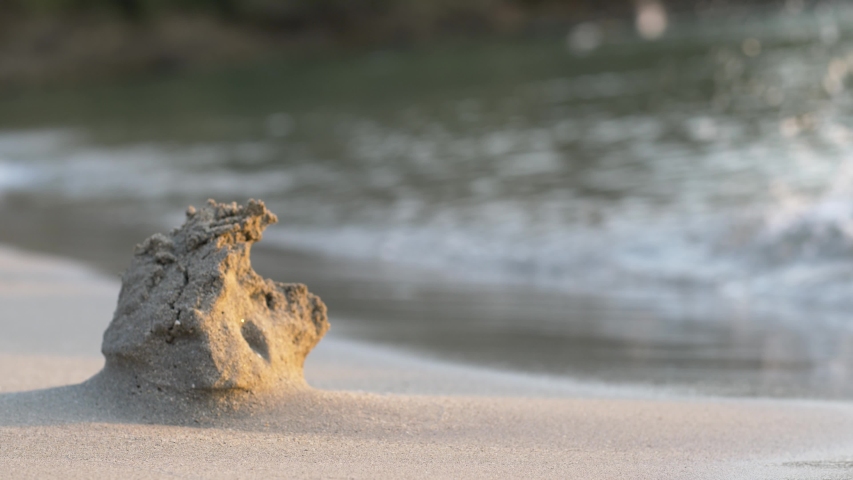 Sand castle/sculpture washing in to the sea as waves slowly eats from it