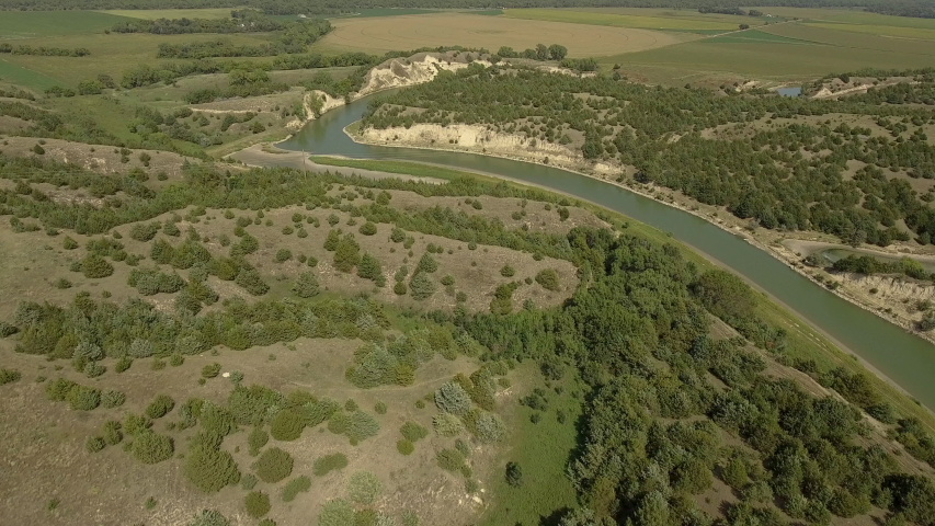 Drone shot flying towards and over a canal (small man-made river) that flows through a small canyon in midwest Nebraska.