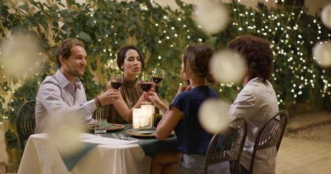 Four people, two couples happy talking and toasting with red wine during a romantic gourmet dinner lunch, party. portrait medium shot.Friends italian trip in Umbria.4k slow motion