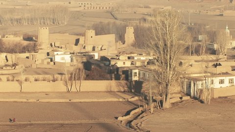 LOCKED OFF view of village in Afghanistan with lone cyclist on path