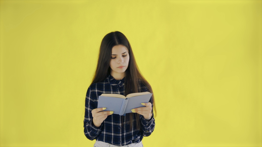 Beautifu thoughtful girl is reading book isolated on yellow background