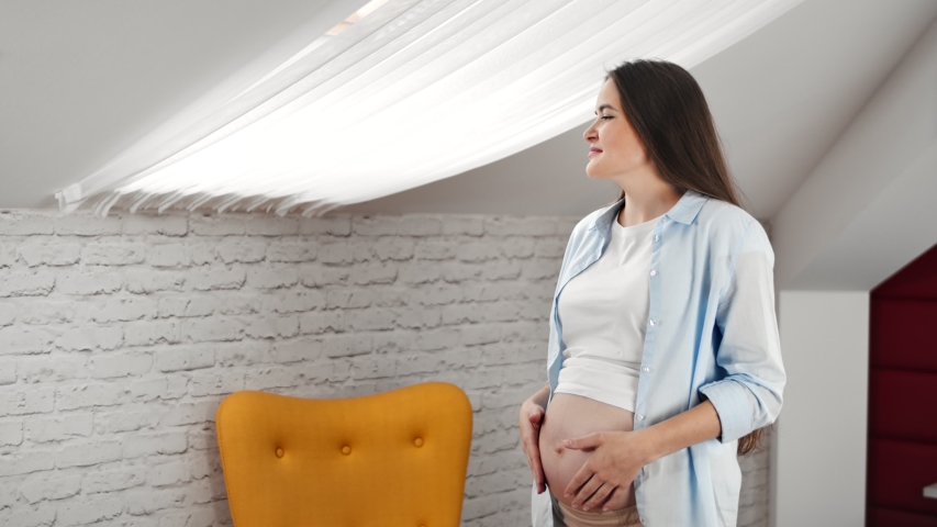 Domestic pregnant young woman dreaming looking out window enjoying weekend at home