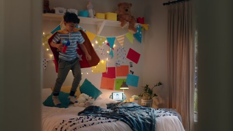 happy little boy jumping on bed wearing costume playing game enjoying playful imagination in colorful bedroom at home