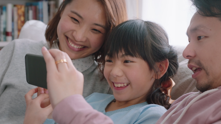 Happy asian family having video chat using smartphone at home mother and father with daughter chatting on mobile phone together waving hand enjoying online communication 4k footage