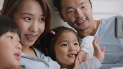 happy asian family having video chat using smartphone in bed mother and father with children waving chatting to friends on mobile phone enjoying online communication 4k footage