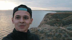 positive young boy doing video selfie (shooting yourself) on the mountain near the sea at sunset